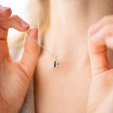 Woman holding the Pure Heart Necklace featuring a delicate heart pendant on a silver chain.